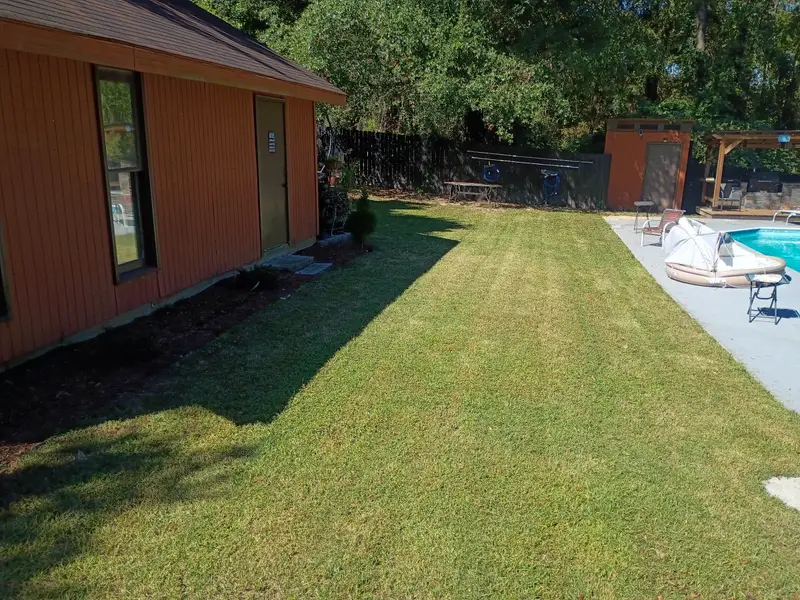 Backyard beside a pool, mowed in stripes with a fresh bed along the house