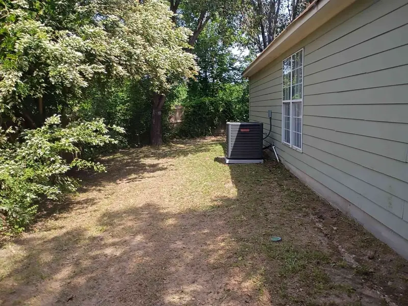 Side yard cleared back toward the fence line beside a green-sided house